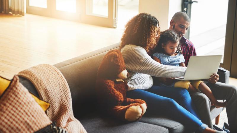 Two parents and their daughter look at a laptop while sitting together on a couch